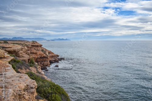 The dry semi-desert of southern Spain meets the blue water of the mediterranean with rocks rising above the water, along the coast of southern Spain
