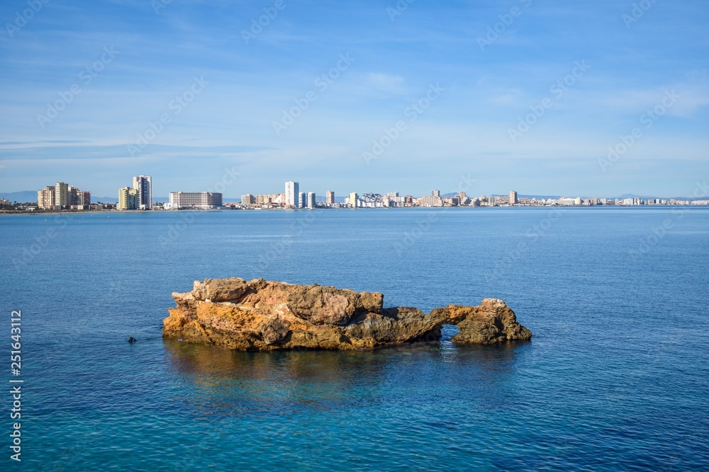 A rugged rocky islet breaks the surface of the calm water of the Mar Minor in La Manga
