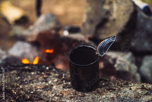 Heating of tea in metal mug on bonfire with large firewood. Tea drinking in open air. Active outdoor recreation. Camping in dusk. Romantic warm atmosphere in twilight on nature. Active rest.
