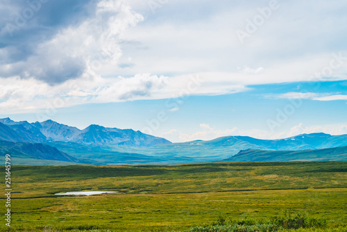 Huge mountain range at overcast weather. Creek and little lake before giant mountains under cloudy sky. Wonderful wild scenery. Dramatic highland landscape of majestic nature. Scenic mountainscape.