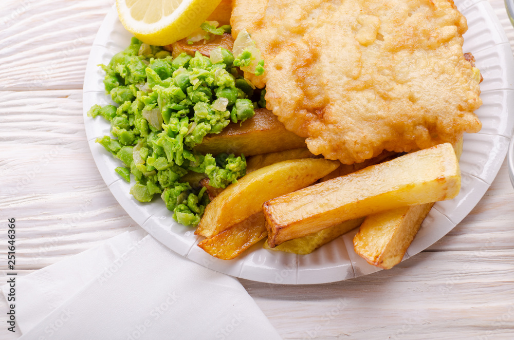 Traditional British street food fish and chips with mushy peas on paper plate