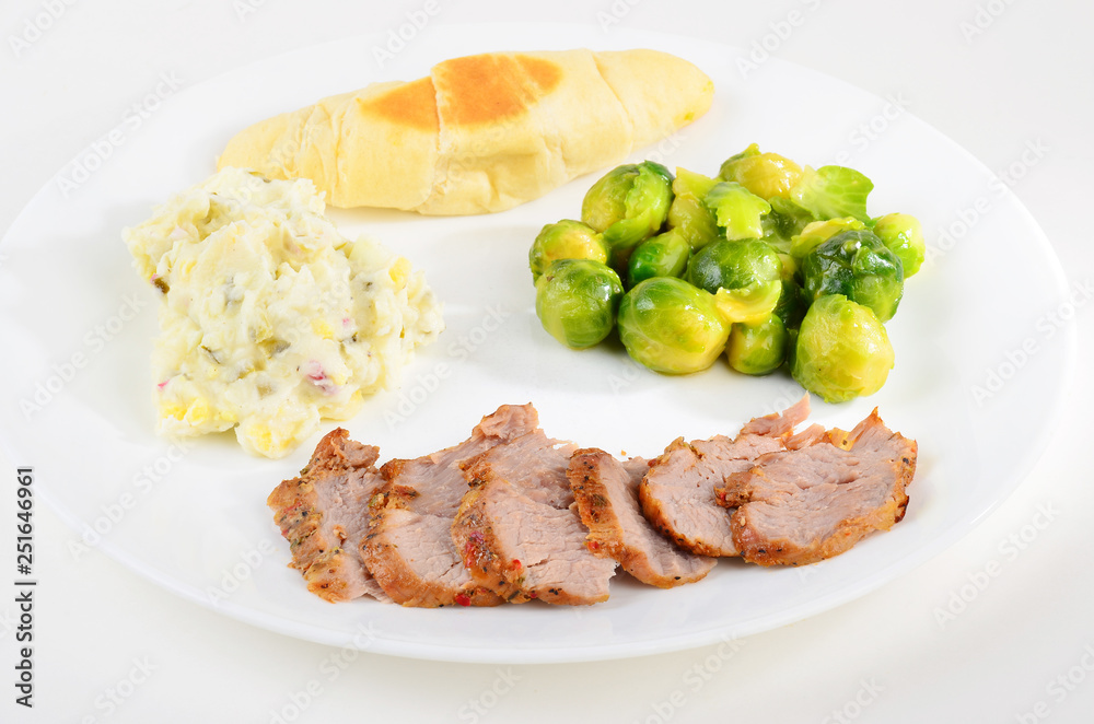 Pork tenderloin and Brussel Sprouts on white plate with potato salad and dinner roll.