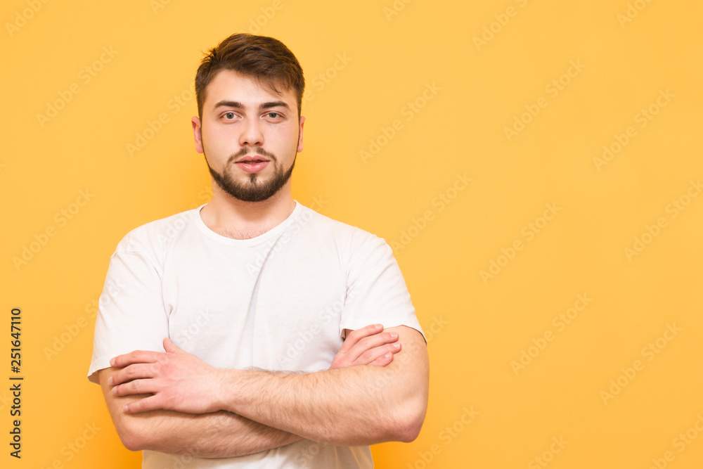 Studio portrait of a bearded man wearing a white T-shirt standing on a yellow background looks at the camera with a serious look. Isolated. Copyspace Studio portrait of a bearded man wearing a white T-shirt standing on a yellow background looks at the camera with a serious look. Isolated. Copyspace