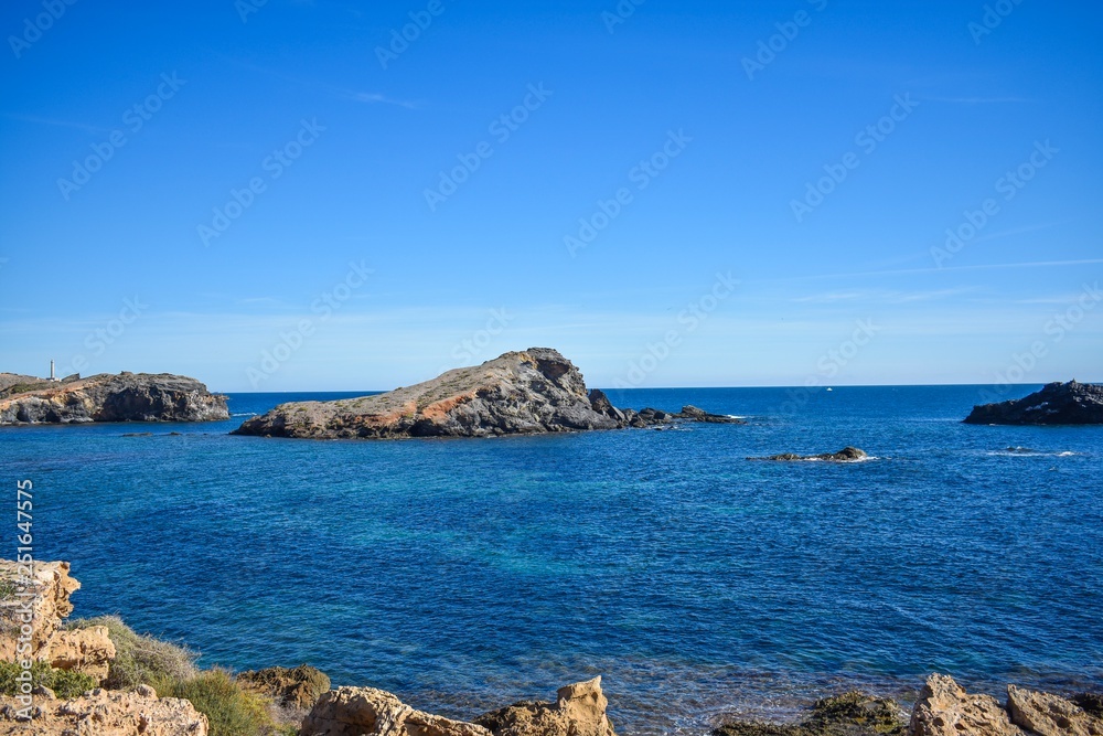 Blue water envelop a dark grey rock or islet, that just rise above the surface along the southern coast of Spain 