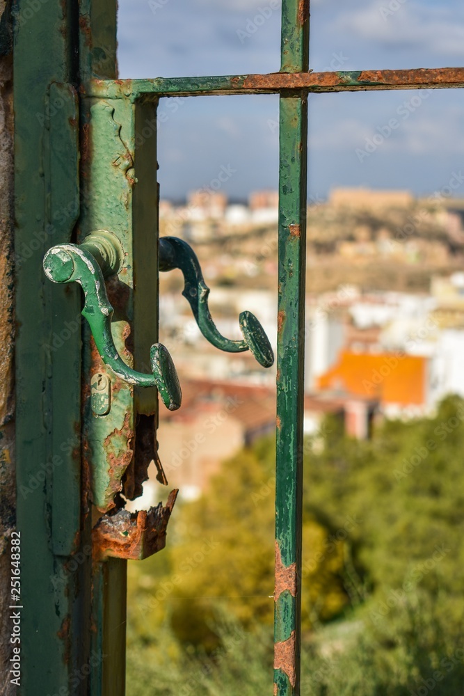 An old rusted gate handle with the blurred view of buildings in the background.