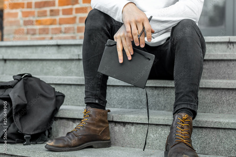 Close up of pensive man sitting on concrete steps and holding notepad in hands. Close up of pensive man sitting on concrete steps and holding notepad in hands.