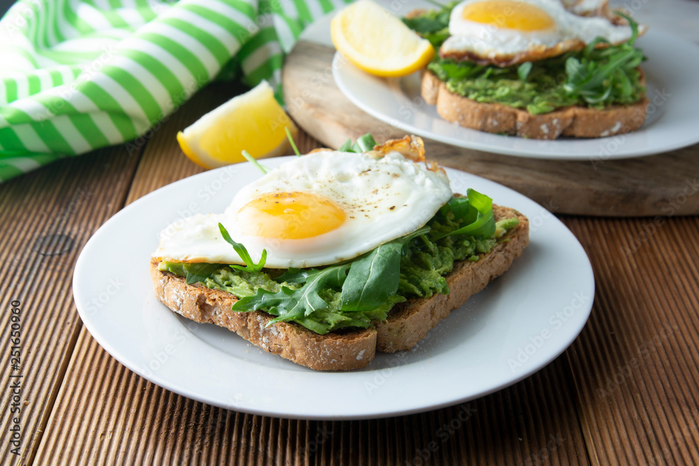 Sandwich or bread toast with avocado and a fried egg on a white plate on rustic wood table. Healthy food. Healthy eating. Sandwich or bread toast with avocado and a fried egg on a white plate on rustic wood table. Healthy food. Healthy eating.