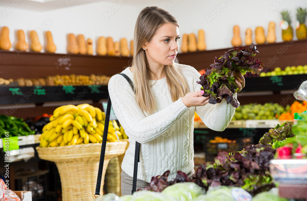 Young woman  customer choosing fresh greens and letuce