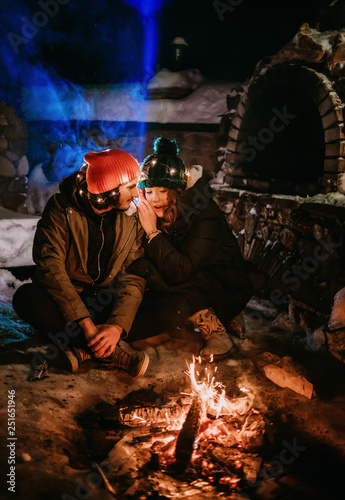 Romantic night. Sparkling guy and the girl are sitting near the fire and exhale blue smoke. 