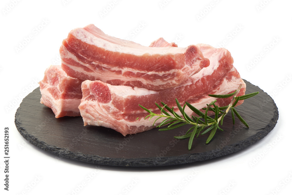 Raw fresh pork ribs with rosemary on a slate shale plate, close-up, isolated on white background