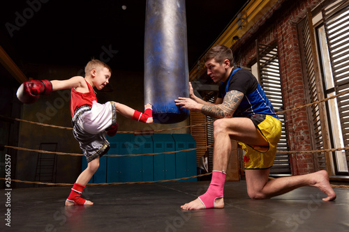 Trainer teaching a kid how to hit punches. Kid wearing boxing gloves and head guard training with his coach inside a boxing ring