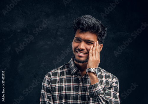 Portrait of a confused Indian young man touching his head. Studio photo against a dark textured wall