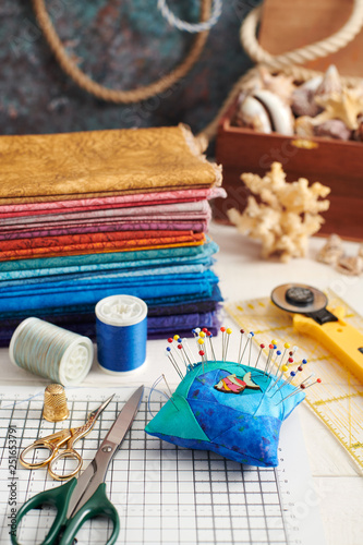 Accessories for quilting and a stack of colorful fabrics for quilting on the background of the box with seashells