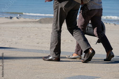 legs of a man and a woman walking in trousers and shoes along the promenade against the sea