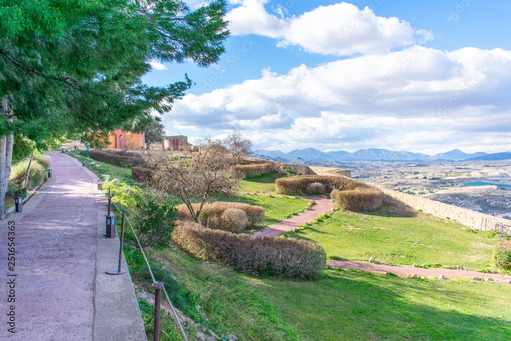 Fototapeta premium The gardens of Lorca Castle in southern Spain, showing walkways that cris-cross the lawn, with a wall on the far-side and the view down below.