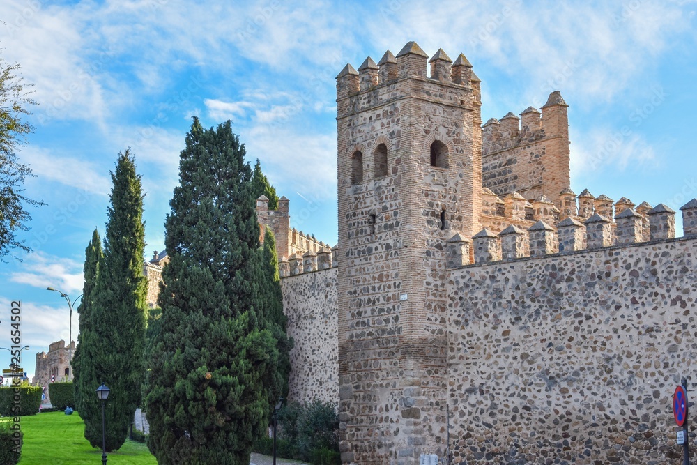 The defensive stone walls of Toledo, Spain, showing the battlements on top and a guard tower with the green lawn that now surrounds the city.
