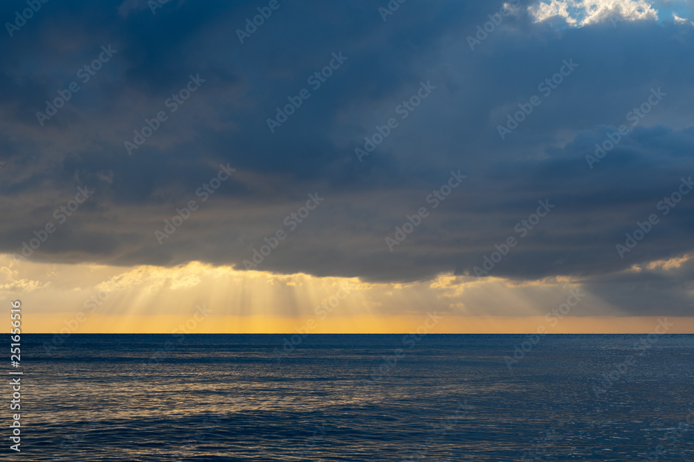 Magnificent cloud burst. Epic scenery of sun rays beaming through heavy rain clouds over the ocean. Low tide, calm waters, sunset. Magnificent cloud burst. Epic scenery of sun rays beaming through heavy rain clouds over the ocean. Low tide, calm waters, sunset.