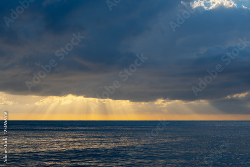 Magnificent cloud burst. Epic scenery of sun rays beaming through heavy rain clouds over the ocean. Low tide  calm waters  sunset.