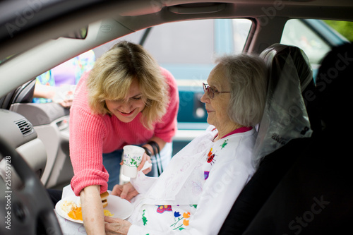 Mid-adult woman reaching over her elderly mother who is sitting inside a car. photo