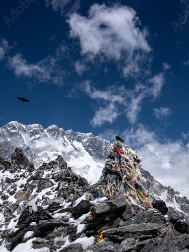 Portrait view of Kongma La pass. Buddhist flags surround the stone marker on the top. Two black birds. Sagarmatha (Everest) National Park, Nepal.