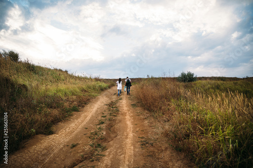 Young family with a small kid walking on the country road back view, outdoors background