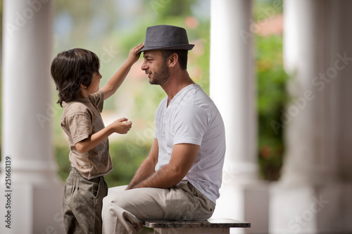 Thirtysomething man sits as his young son plays with his trilby hat. photo