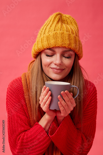 Beautiful teenage girl in warm cozy sweater with cup of hot drink. Red background. Studio