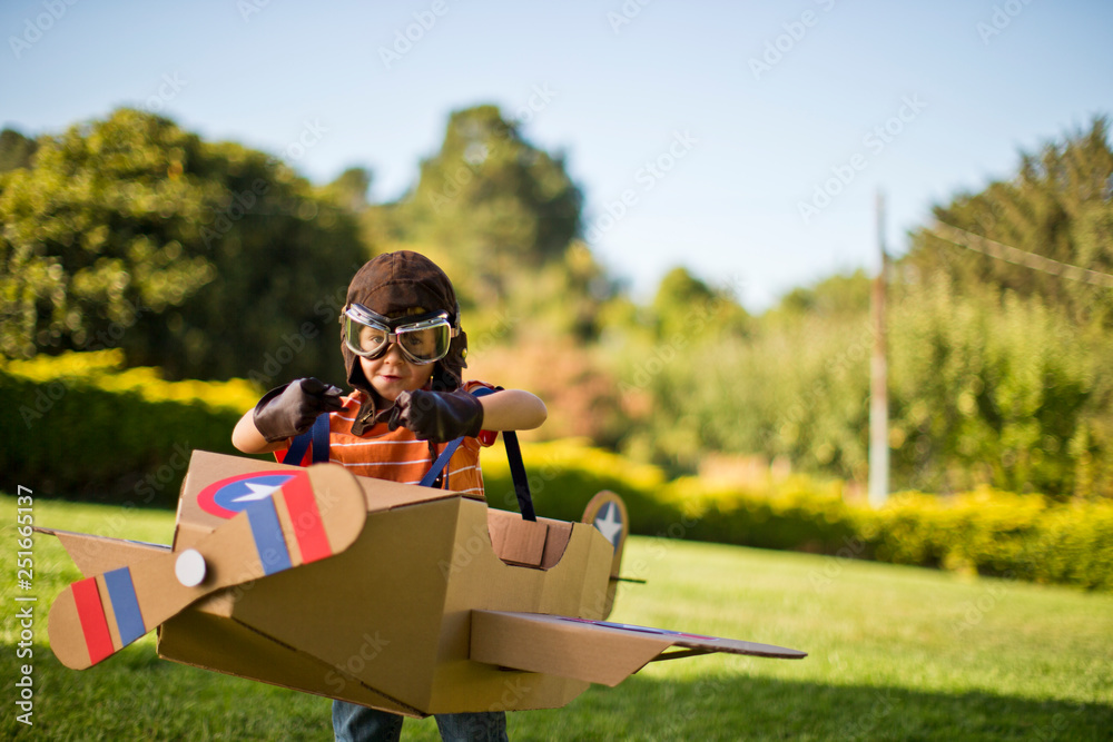 Young boy having fun pretending to be a pilot in a cardboard plane.