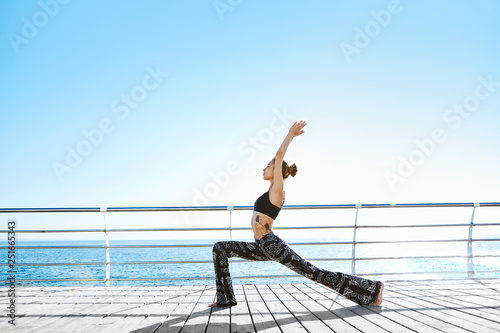 Photo of young sports woman make yoga exercises on seaside.