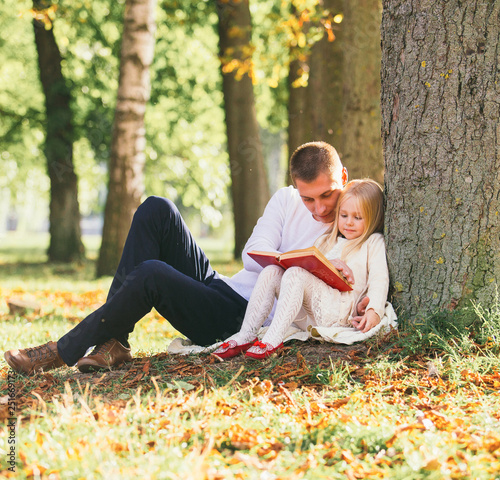 Cute little blonde girl sit near tree with father, read favorite book and dream © kozirsky