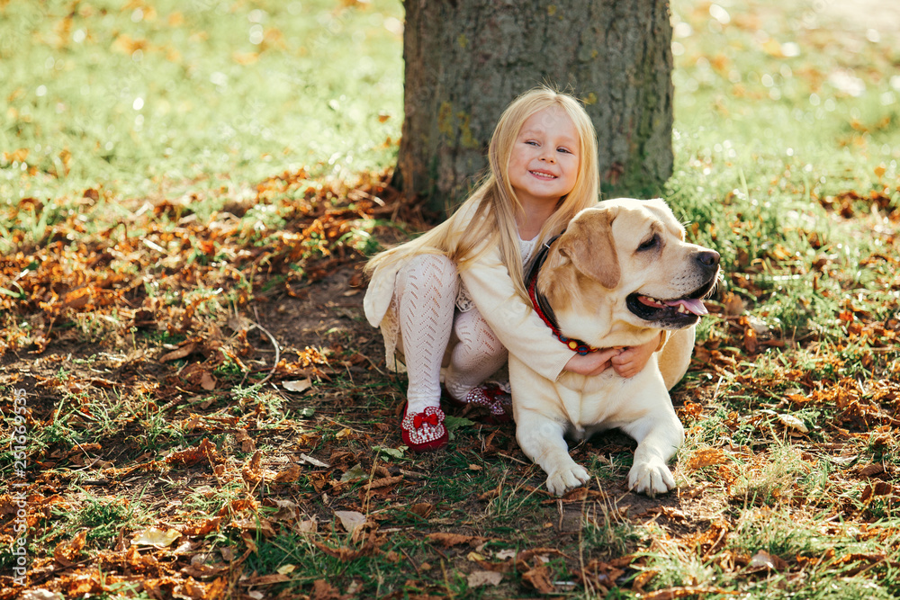 Cute little blonde girl sitting with dog on the grass in the forest