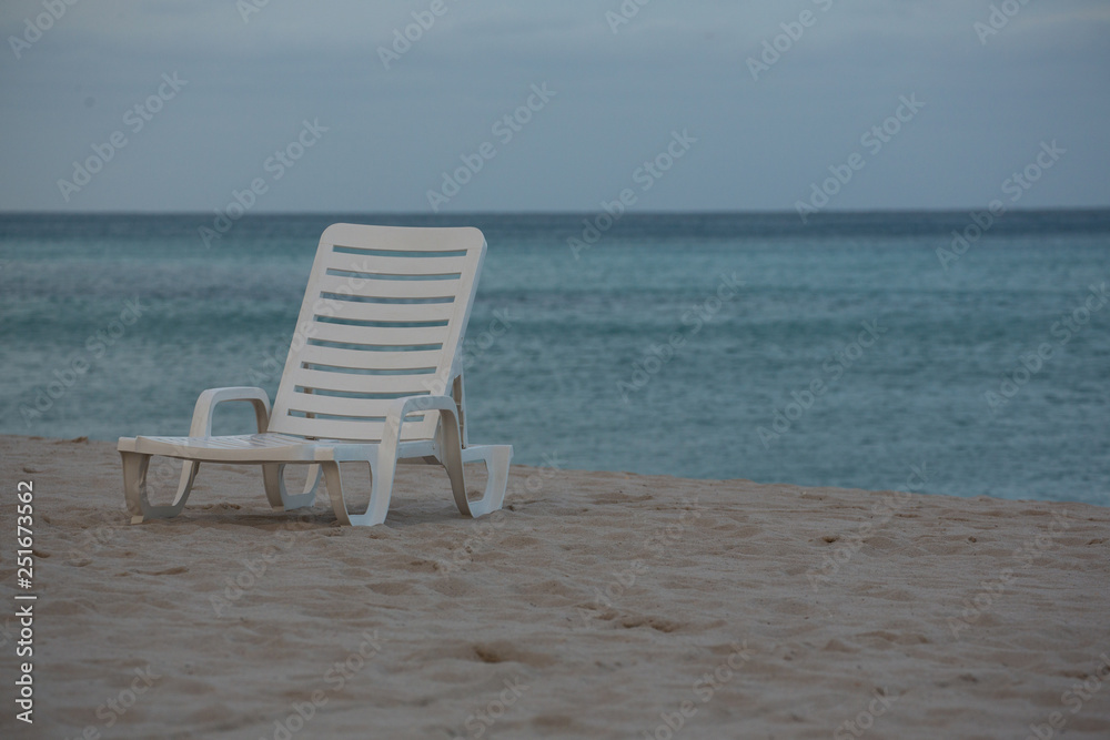 A White Beach Chair on the Beautiful Sunset Beach. Ahtlantic Ocean on a Background A White Beach Chair on the Beautiful Sunset Beach. Ahtlantic Ocean on a Background