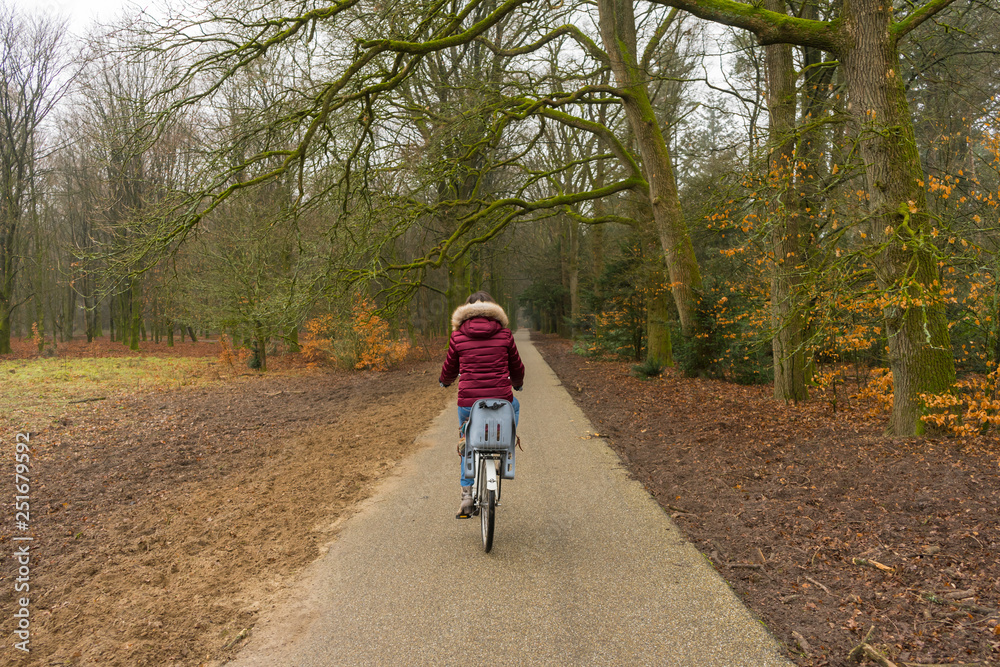 Single woman riding a bike trought straight tree path inside the woods. 
