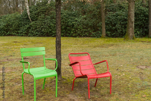 Green and Red sit chair standing next to eachother on green grass with one trees in the background nature.