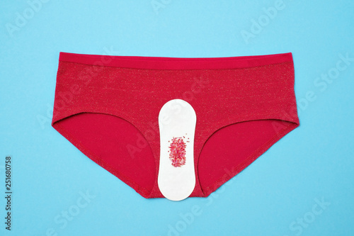 Red drop from beads on pants on blue background. Menstruation period photo