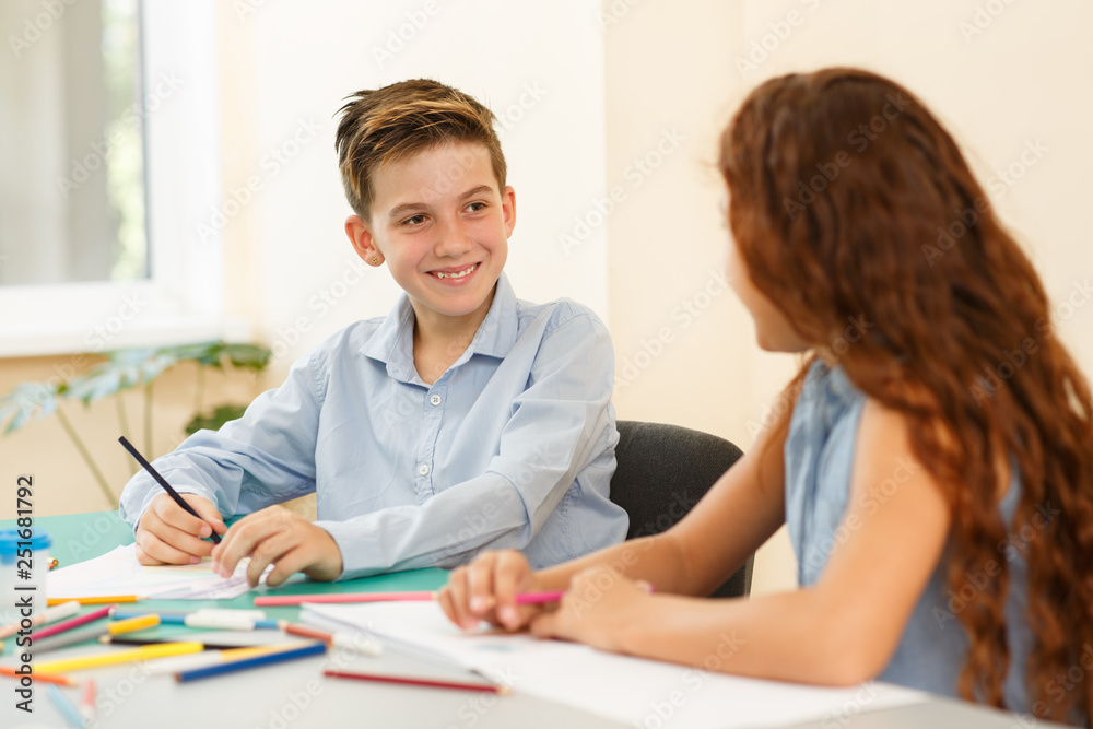 ?ute boy sitting at desk and looking at girl sitting next to him. ?ute boy sitting at desk and looking at girl sitting next to him.