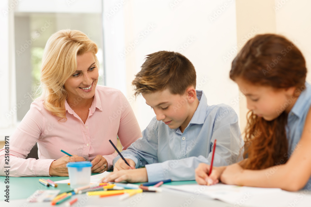Pupils with female teacher sitting at desk with many pencil on and painting on paper. One little cute boy leaning on hand, smiling and looking at camera during art lesson. Pupils with female teacher sitting at desk with many pencil on and painting on paper. One little cute boy leaning on hand, smiling and looking at camera during art lesson.
