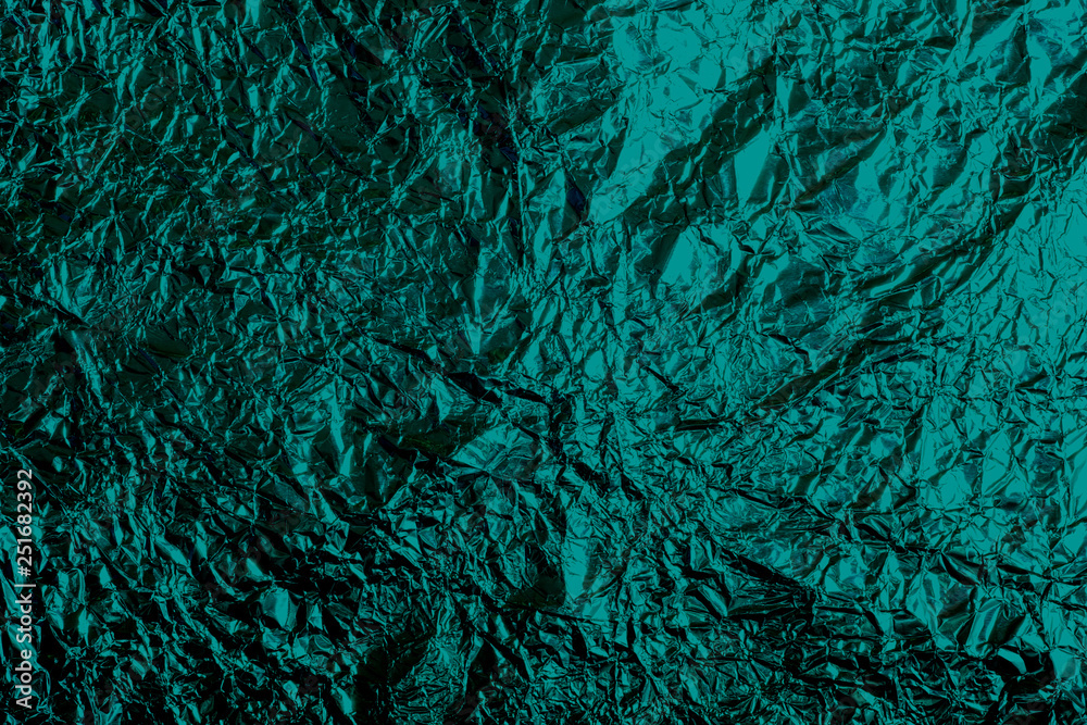 Thin sheet of emerald color foil paper background with shiny uneven surface. 