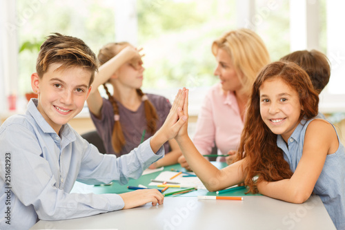 Cute boy giving high five to his classmates sitting opposite.