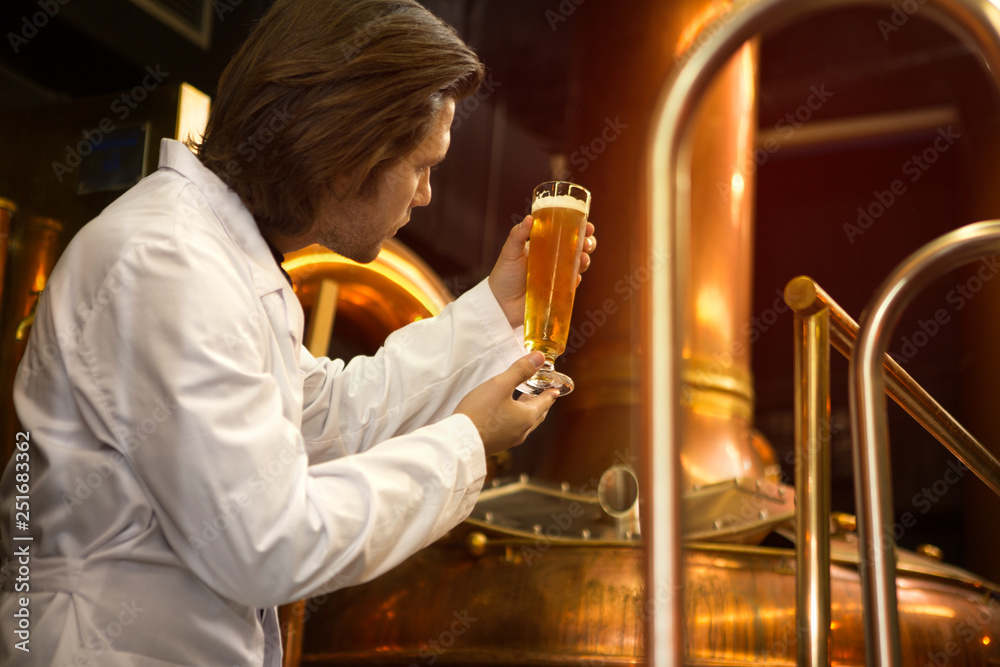 Specialist of brew industry holding glass of beer in hands and looking