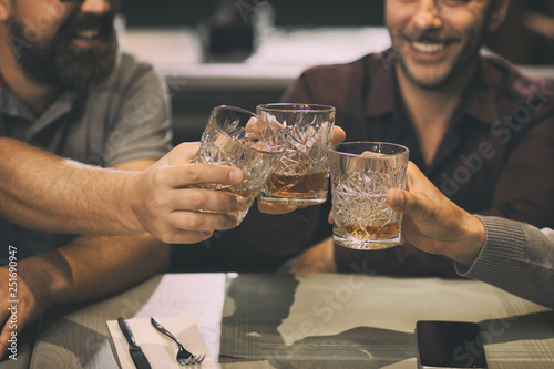 Close up of unrecognizable men clinking crystal glasses with alcoholic beverage. Clients of bar or pub enjoying their drinks such as whiskey, rum, scotch or brandy.