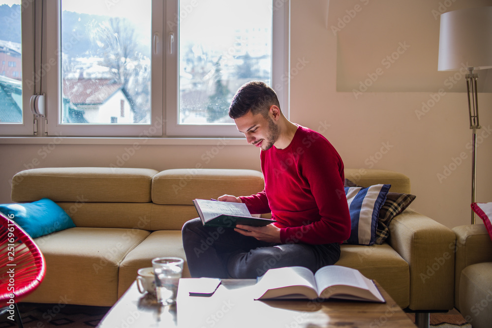 Attractive young man relaxing with a book at home sitting on the sofa Attractive young man relaxing with a book at home sitting on the sofa
