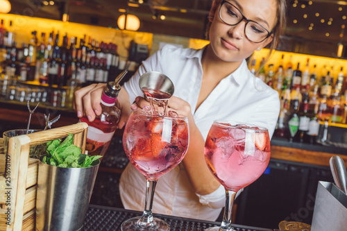 female beautiful smart bartender mixologist bar person makes prepares gin tonic cocktail drink pink mint fish bowl glass photo