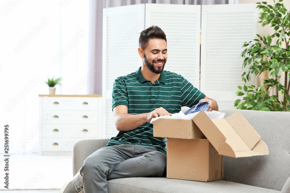 Young man opening parcel on sofa at home Young man opening parcel on sofa at home