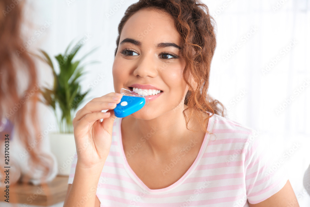 Young African-American woman using teeth whitening device at home Young African-American woman using teeth whitening device at home