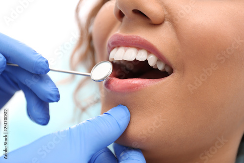 Dentist examining African-American woman's teeth with mirror, closeup