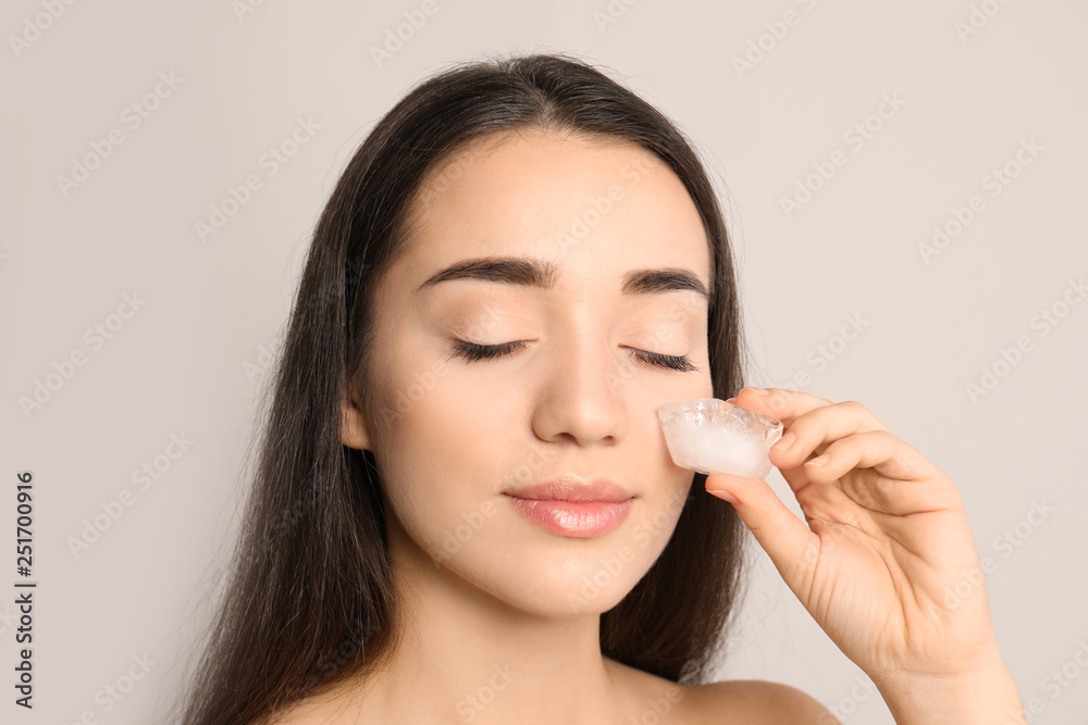 Young woman with ice cube on light background. Skin care