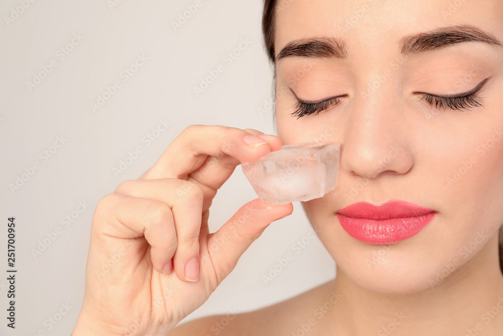 Young woman with ice cube on light background. Skin care