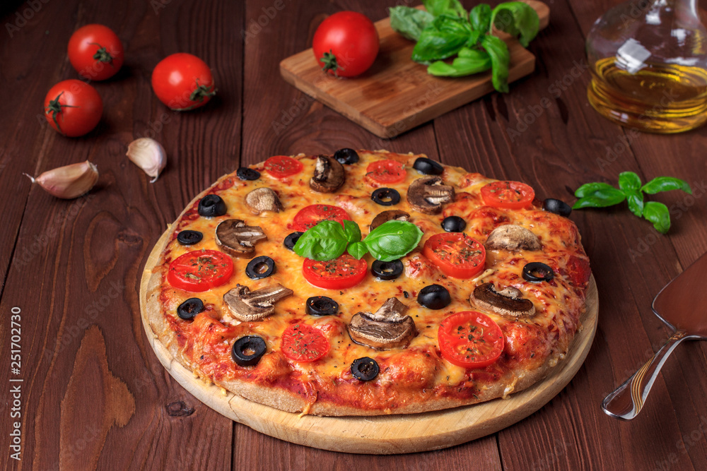 Traditional Italian vegetarian pizza with mushrooms, cherry tomatoes, black olives and basil on brown wooden table