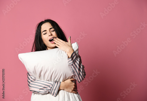 Beautiful brunette girl just woke up with soft pillow and feathers. Woman yawning sleepy day on pink